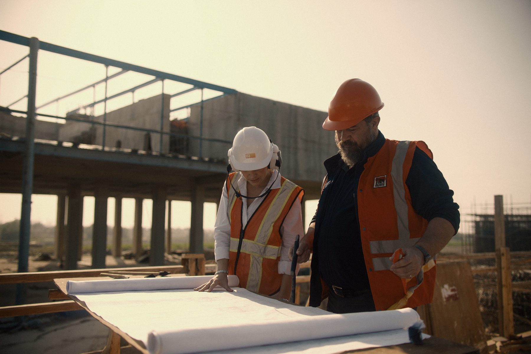 Two engineers in hard hats studying a technical drawing together on site.